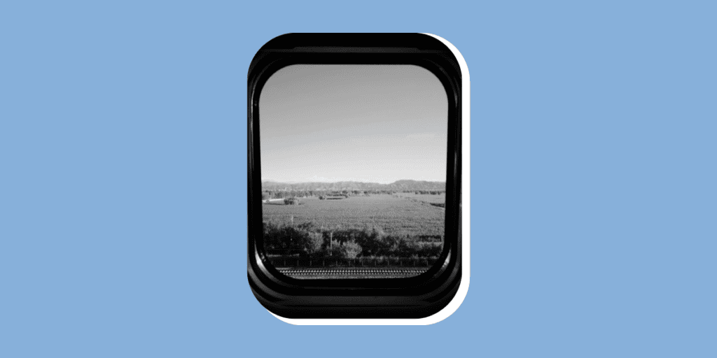 A landscape view of fields and distant mountains seen through a train window, with the photo in black and white.